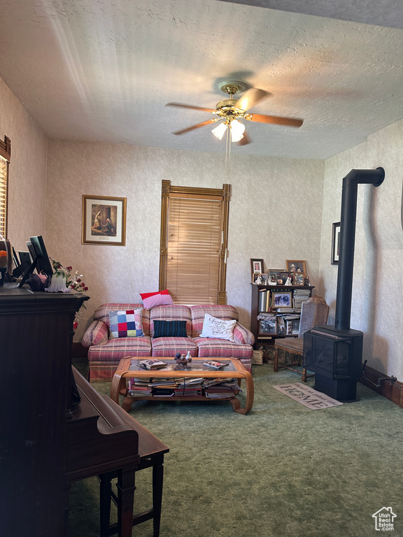 Living room featuring a wood stove, carpet flooring, and ceiling fan