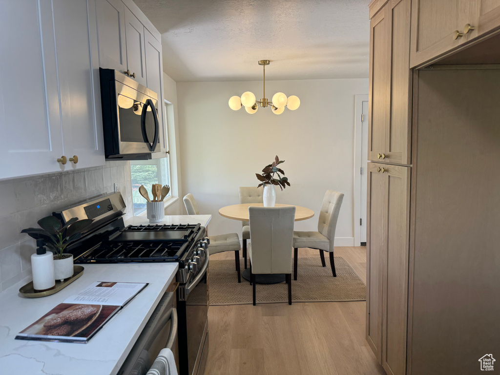 Kitchen featuring stainless steel appliances, a chandelier, light wood-style flooring, tasteful backsplash, and light countertops