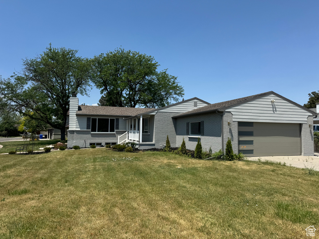 Ranch-style home featuring brick siding, a garage, a chimney, a front yard, and driveway