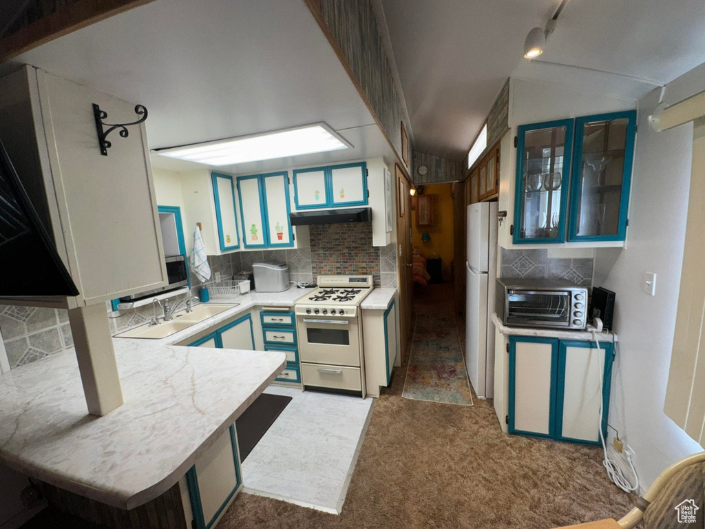 Kitchen featuring white appliances, under cabinet range hood, light countertops, backsplash, and carpet flooring