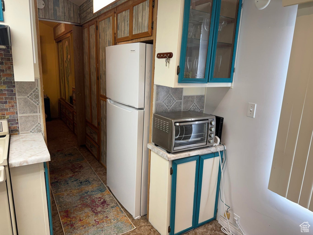Kitchen featuring freestanding refrigerator, backsplash, light countertops, and glass insert cabinets