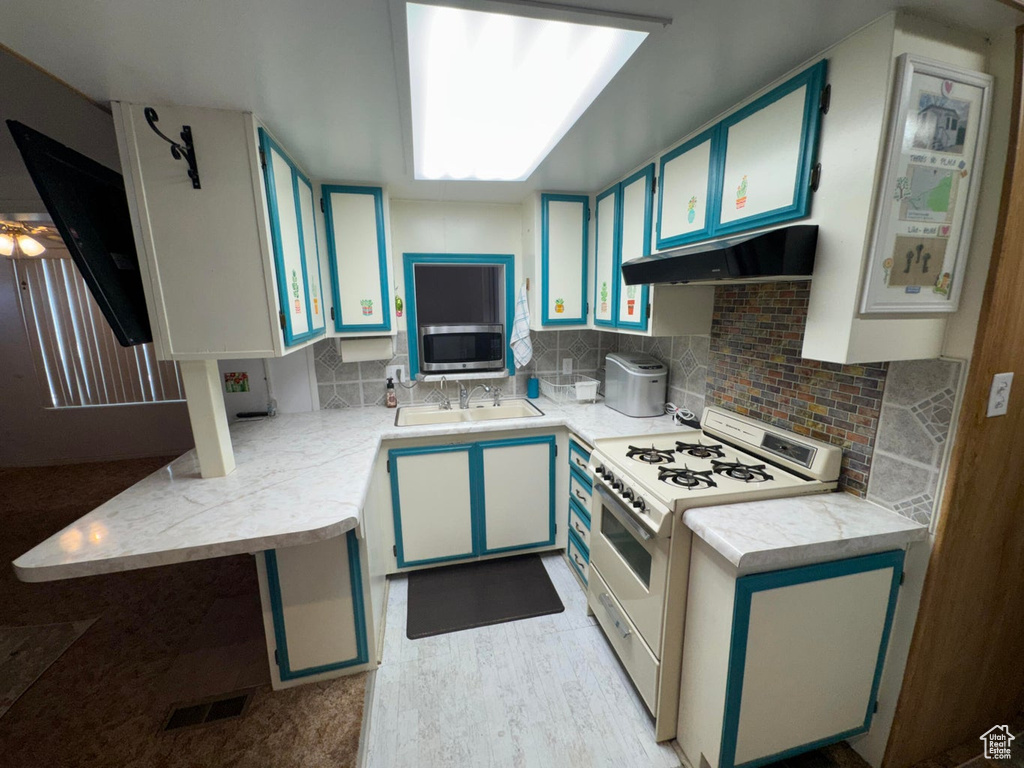 Kitchen with white range with gas cooktop, under cabinet range hood, light countertops, stainless steel microwave, and backsplash