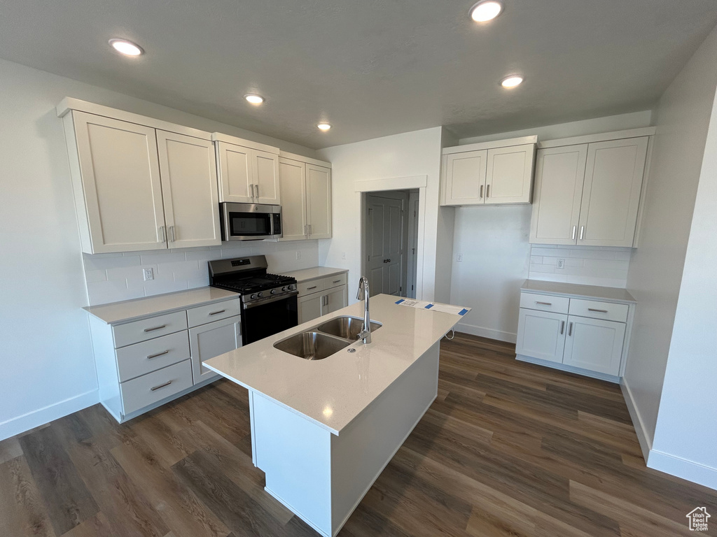 Kitchen with stainless steel appliances, tasteful backsplash, a center island with sink, dark wood finished floors, and recessed lighting