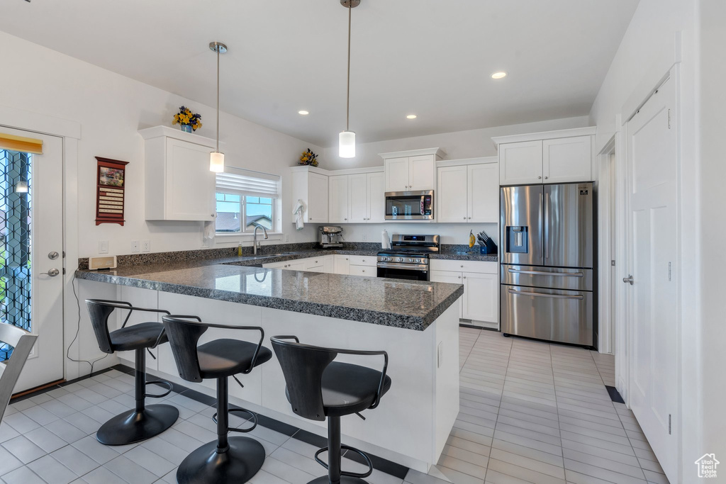 Kitchen with appliances with stainless steel finishes, a peninsula, white cabinets, a breakfast bar, and recessed lighting