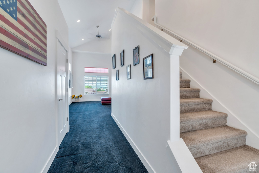 Corridor featuring dark colored carpet, stairs, high vaulted ceiling, and recessed lighting