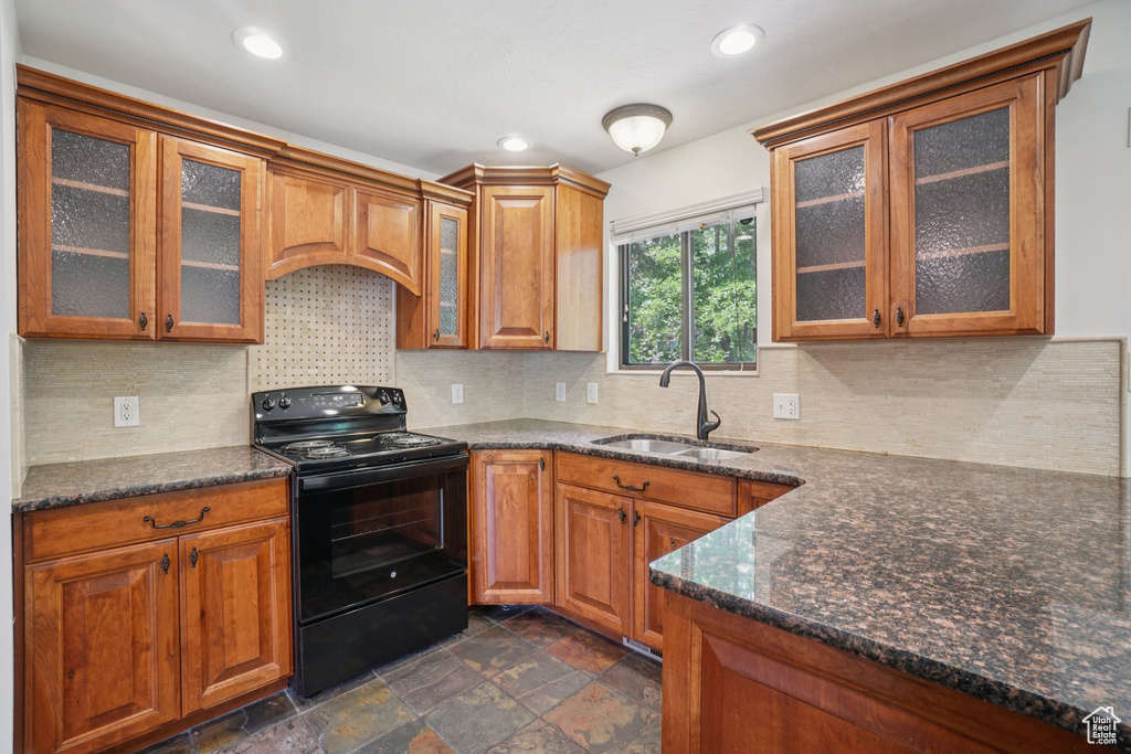 Kitchen featuring black electric range oven, brown cabinetry, glass insert cabinets, and recessed lighting