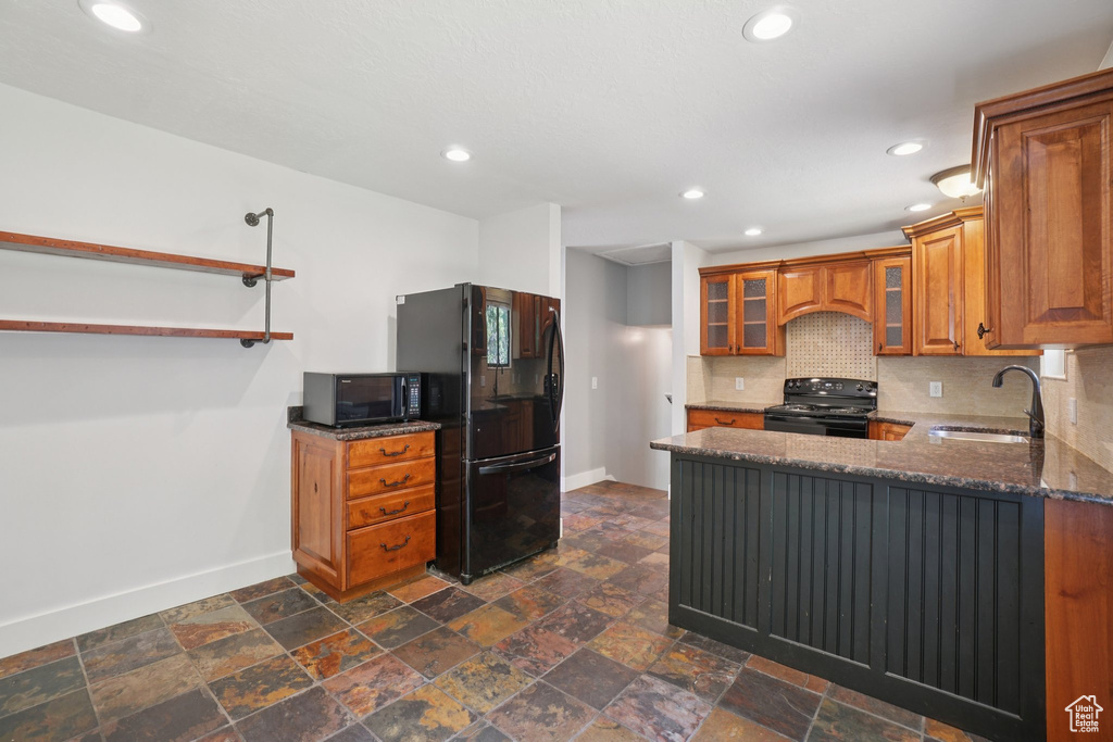 Kitchen with black appliances, brown cabinets, dark stone countertops, tasteful backsplash, and a peninsula