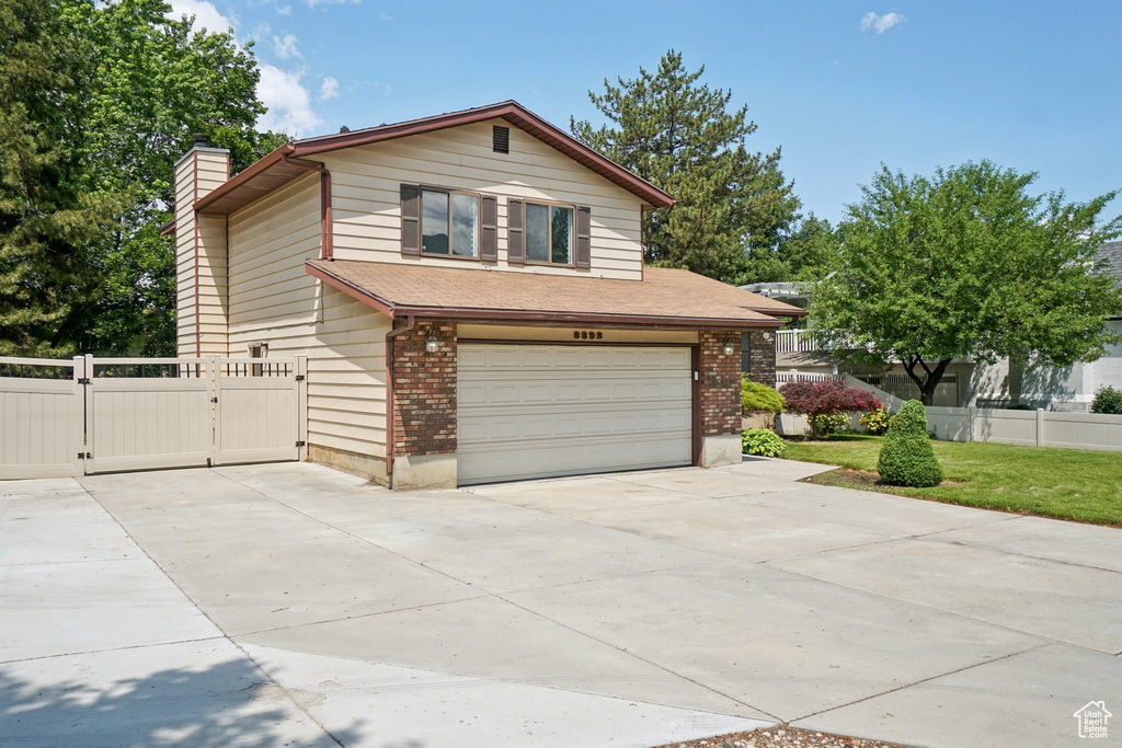 View of front facade featuring a garage, driveway, a gate, a chimney, and brick siding