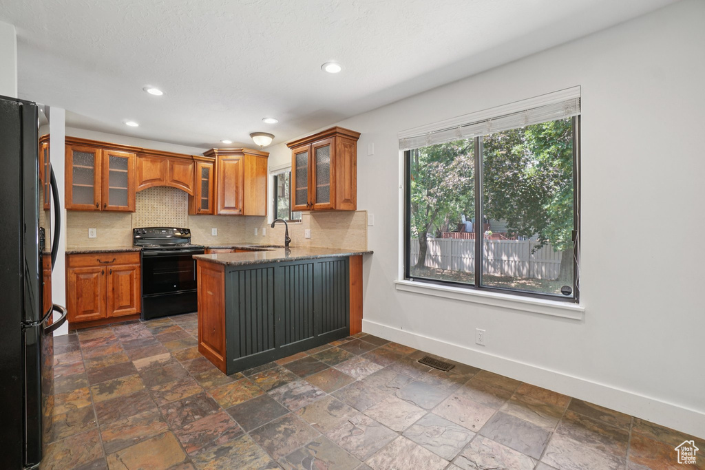 Kitchen with black appliances, a peninsula, brown cabinets, tasteful backsplash, and stone tile floors