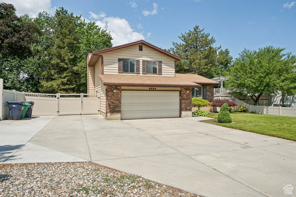 Split level home featuring a gate, an attached garage, driveway, and brick siding