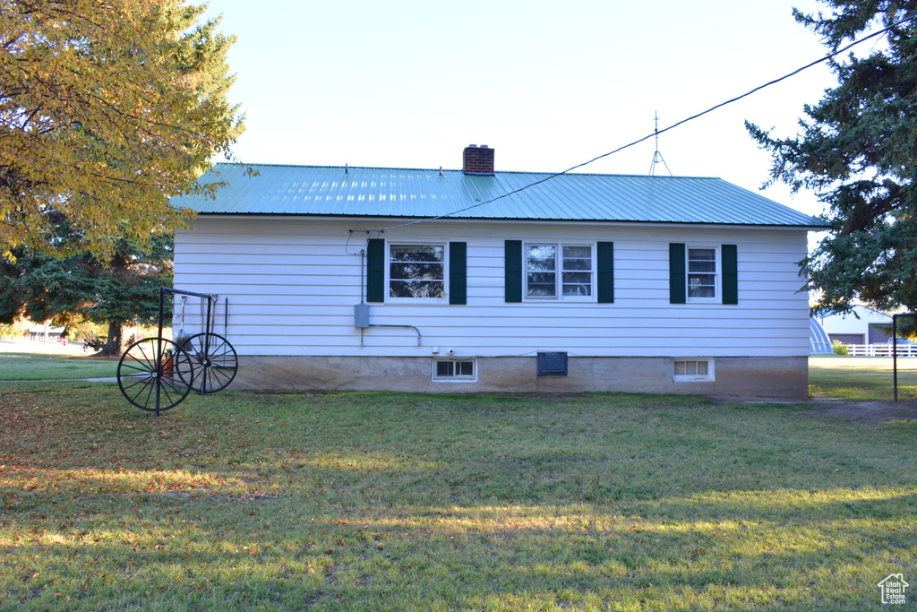 Back of house featuring a chimney, a lawn, and a metal roof
