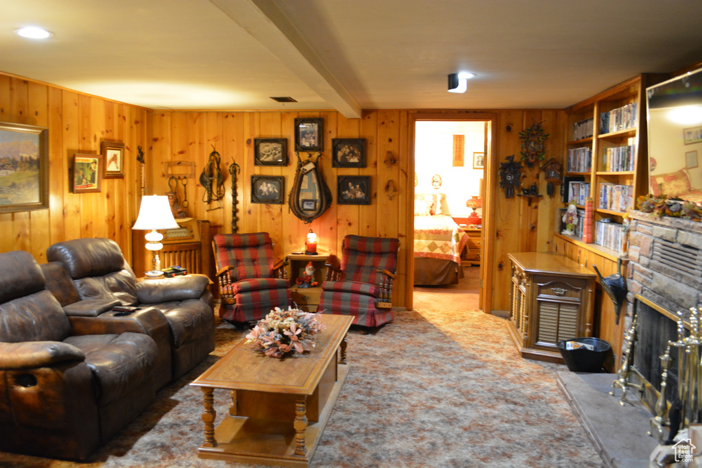 Carpeted living area featuring wood walls, a stone fireplace, and beamed ceiling