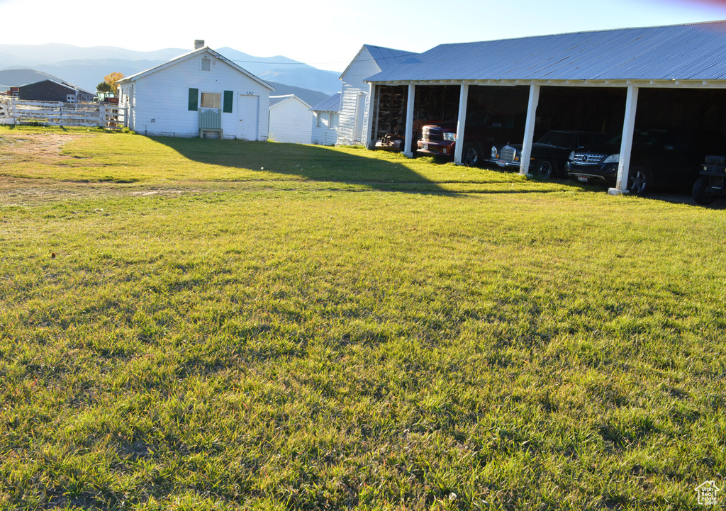 View of grassy yard featuring a mountain view, a carport, and a pole building