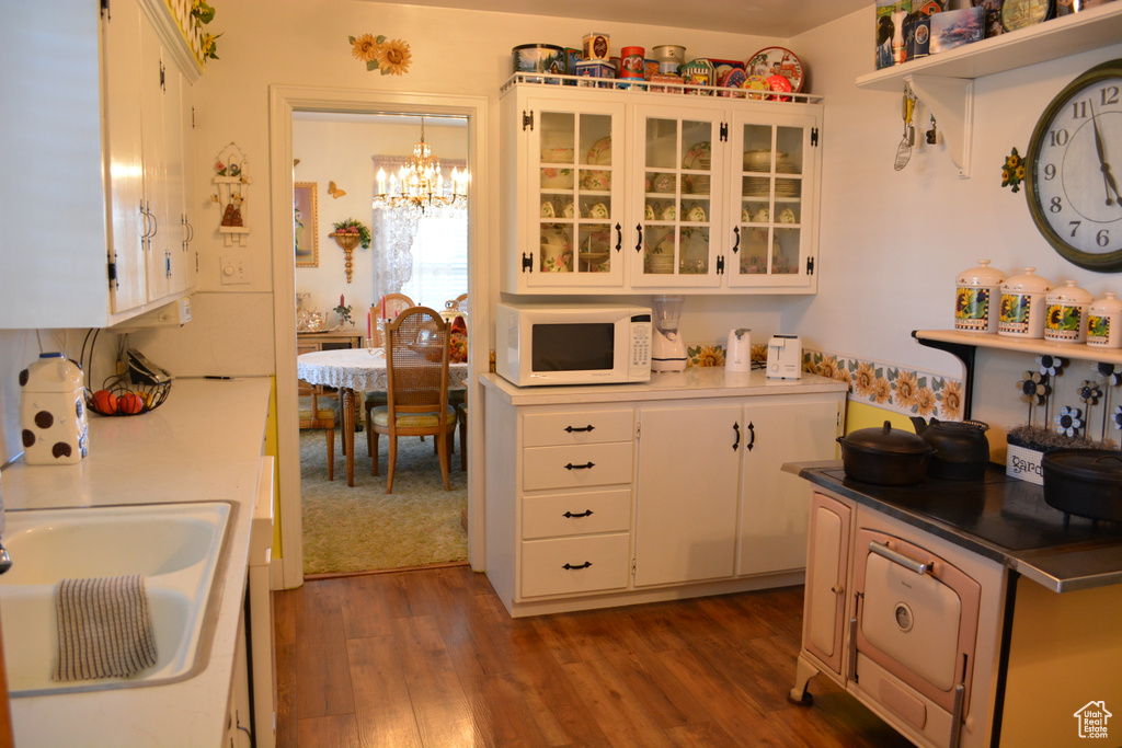 Kitchen with white microwave, a chandelier, dark wood-style flooring, white cabinets, and glass insert cabinets