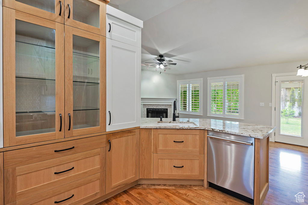 Kitchen with dishwasher, light wood-style floors, ceiling fan, light stone counters, and a peninsula