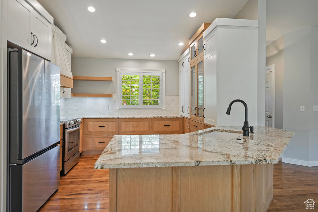 Kitchen with appliances with stainless steel finishes, wood finished floors, recessed lighting, decorative backsplash, and light stone counters