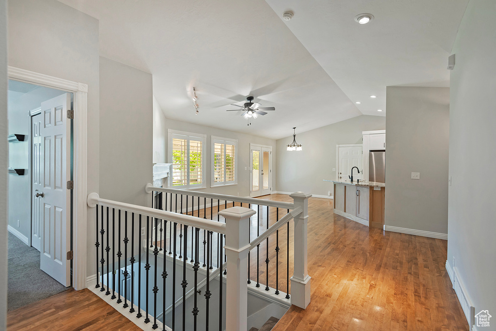Hallway with an upstairs landing, light wood-style floors, vaulted ceiling, and a chandelier