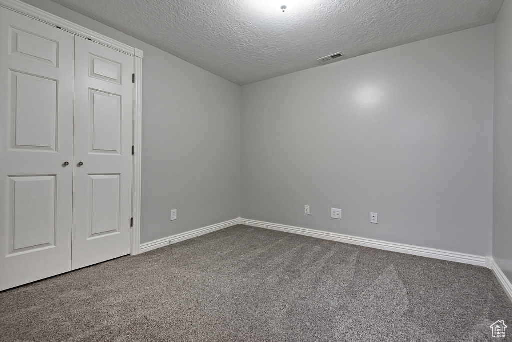 Unfurnished bedroom with dark colored carpet, a textured ceiling, and a closet
