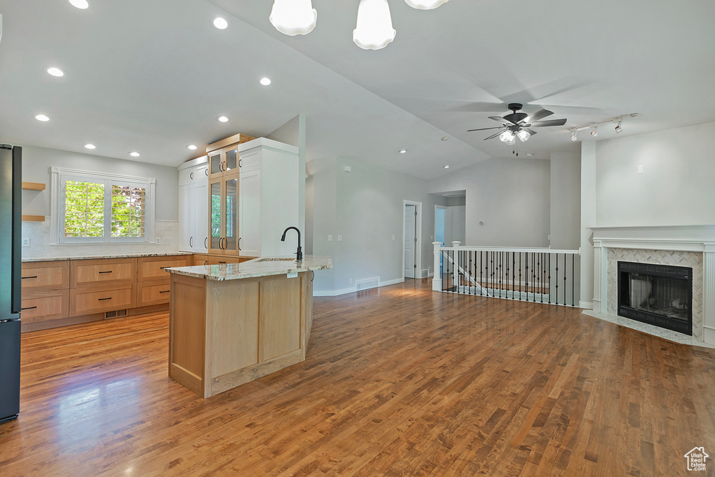 Kitchen featuring open floor plan, ceiling fan, light brown cabinets, vaulted ceiling, and light stone countertops