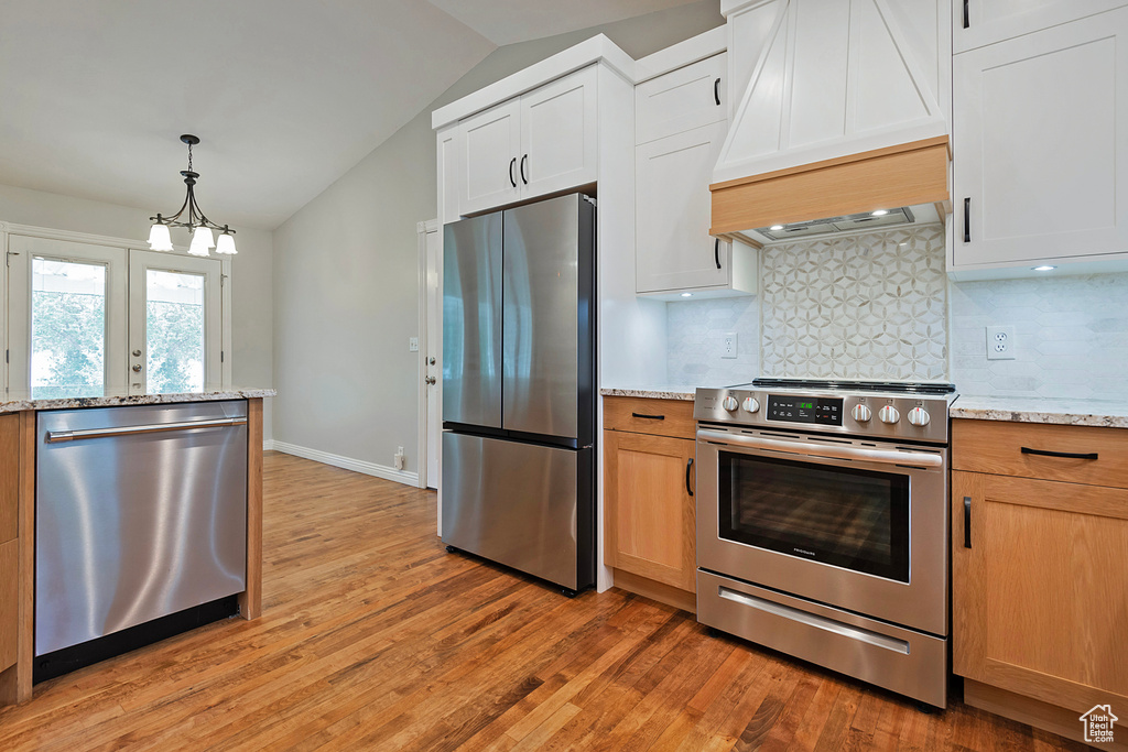 Kitchen featuring appliances with stainless steel finishes, custom exhaust hood, lofted ceiling, light wood finished floors, and decorative backsplash