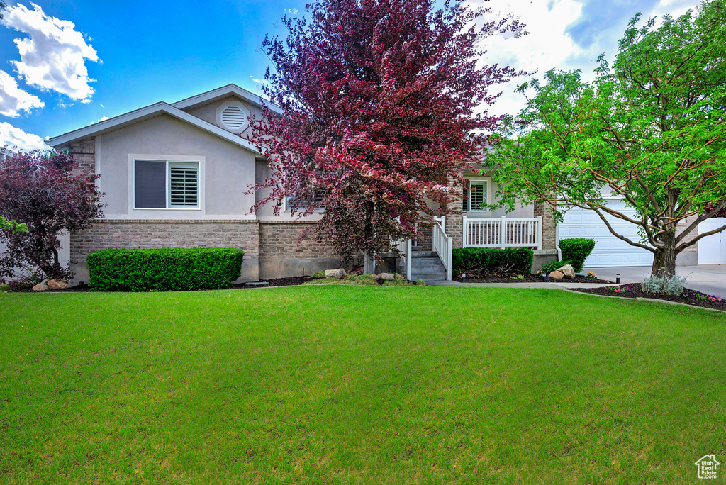 View of front of house featuring an attached garage, stucco siding, a front yard, concrete driveway, and brick siding