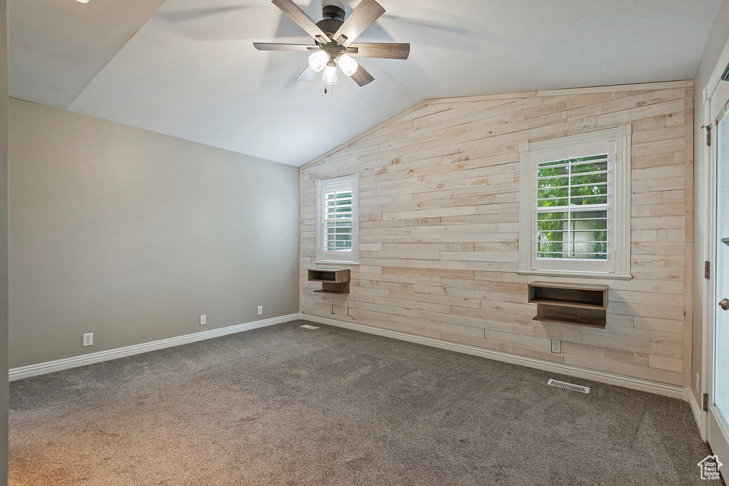 Empty room featuring vaulted ceiling, wood walls, carpet floors, and ceiling fan