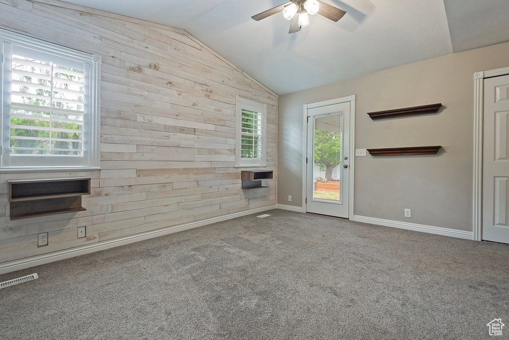 Unfurnished living room featuring lofted ceiling, wood walls, a ceiling fan, plenty of natural light, and carpet floors