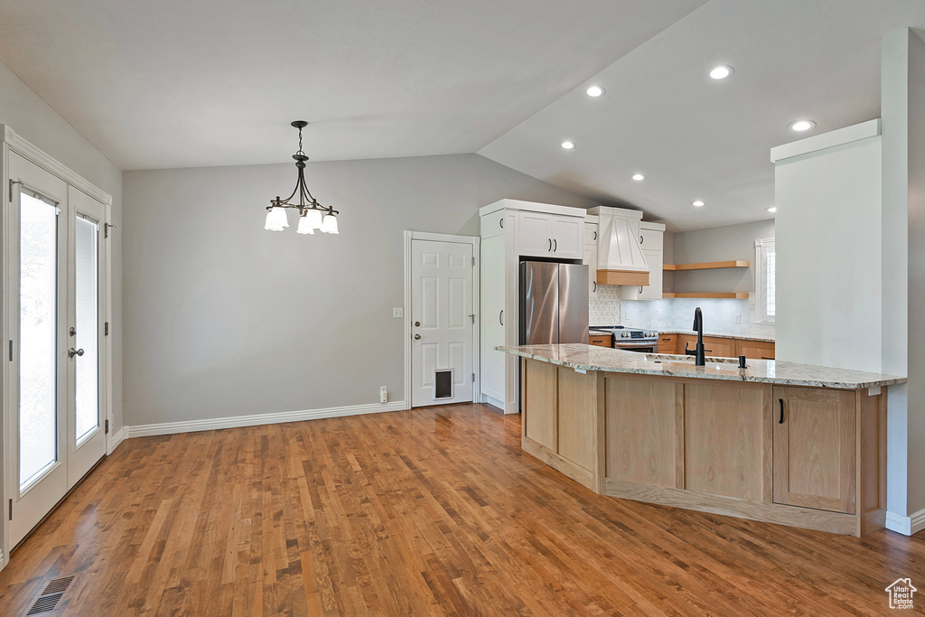Kitchen featuring stainless steel appliances, light stone countertops, a peninsula, lofted ceiling, and light wood-style floors