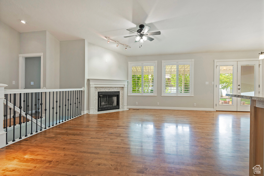 Unfurnished living room featuring a ceiling fan, wood finished floors, track lighting, a glass covered fireplace, and french doors