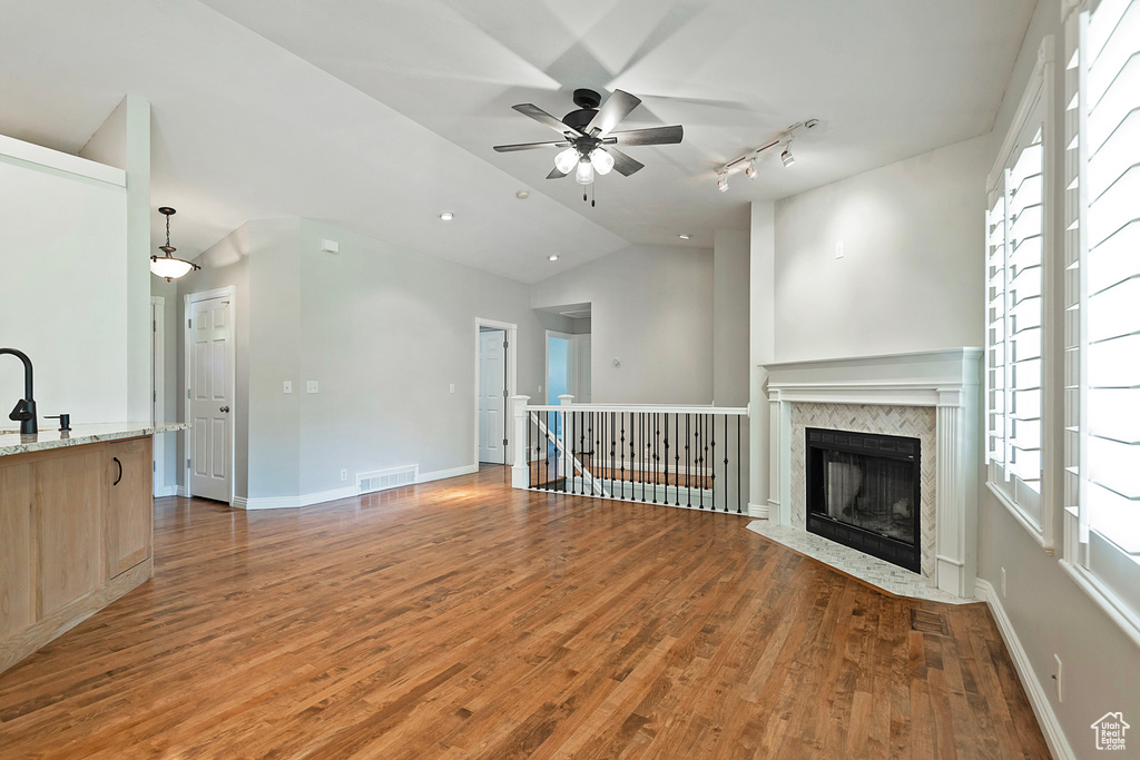 Unfurnished living room with vaulted ceiling, ceiling fan, wood finished floors, healthy amount of natural light, and a fireplace with flush hearth