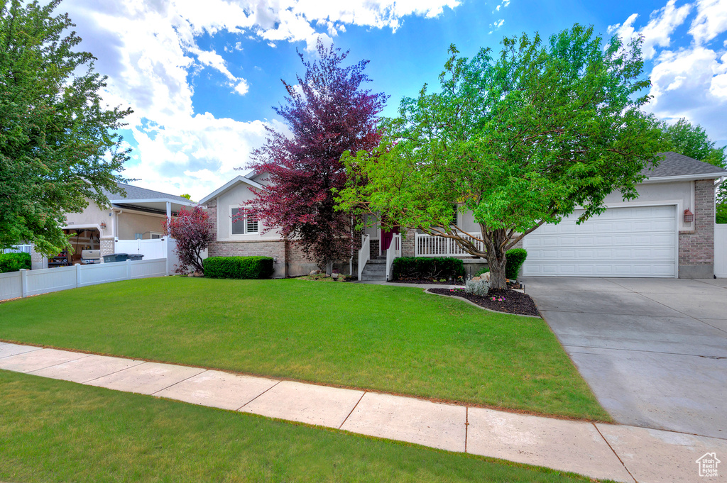 View of property hidden behind natural elements featuring driveway, an attached garage, and brick siding