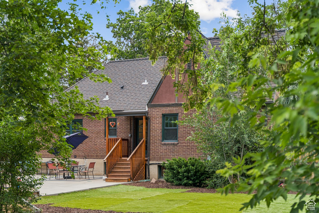 View of front of house featuring brick siding, a front lawn, a patio, and a shingled roof