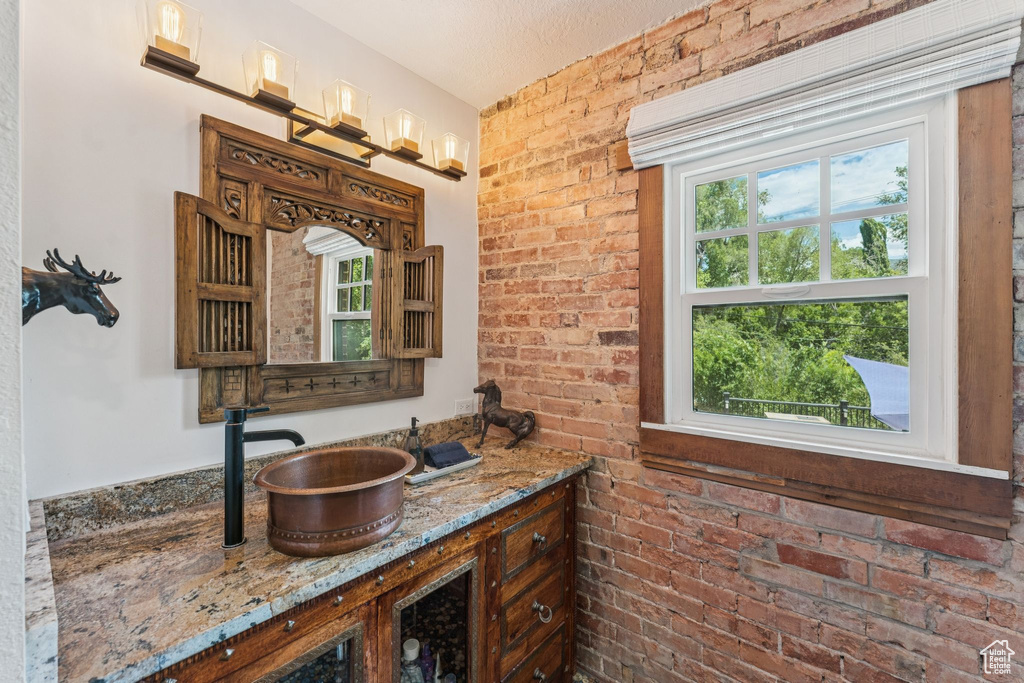Bathroom with healthy amount of natural light, vanity, and brick wall