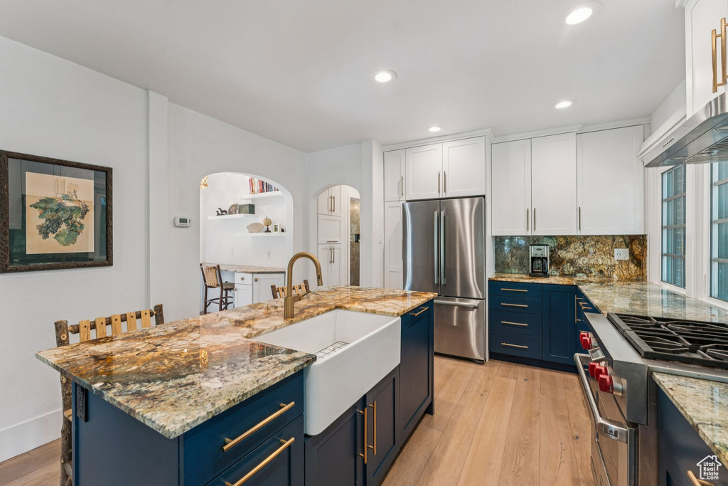 Kitchen with appliances with stainless steel finishes, blue cabinets, white cabinetry, tasteful backsplash, and recessed lighting