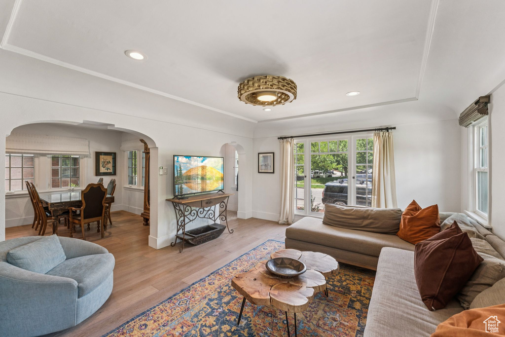 Living area with arched walkways, light wood finished floors, recessed lighting, and a tray ceiling