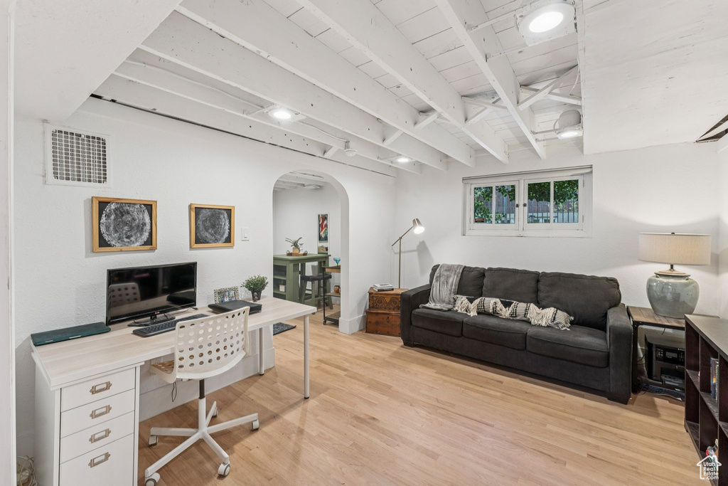 Office area featuring arched walkways, light wood-style floors, and beamed ceiling