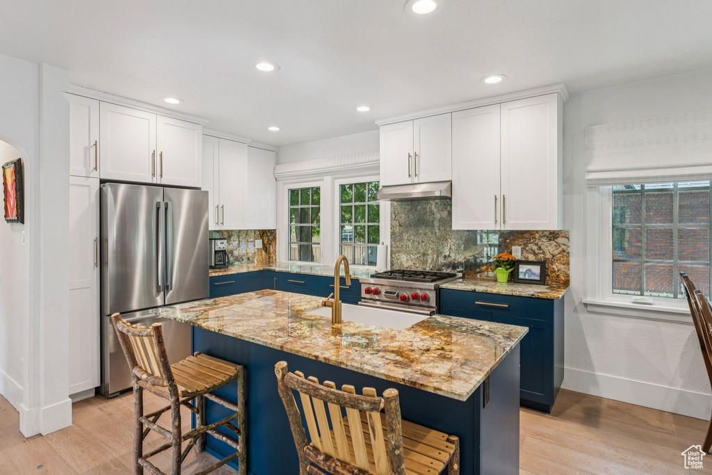 Kitchen featuring stainless steel appliances, under cabinet range hood, light wood finished floors, a kitchen bar, and recessed lighting