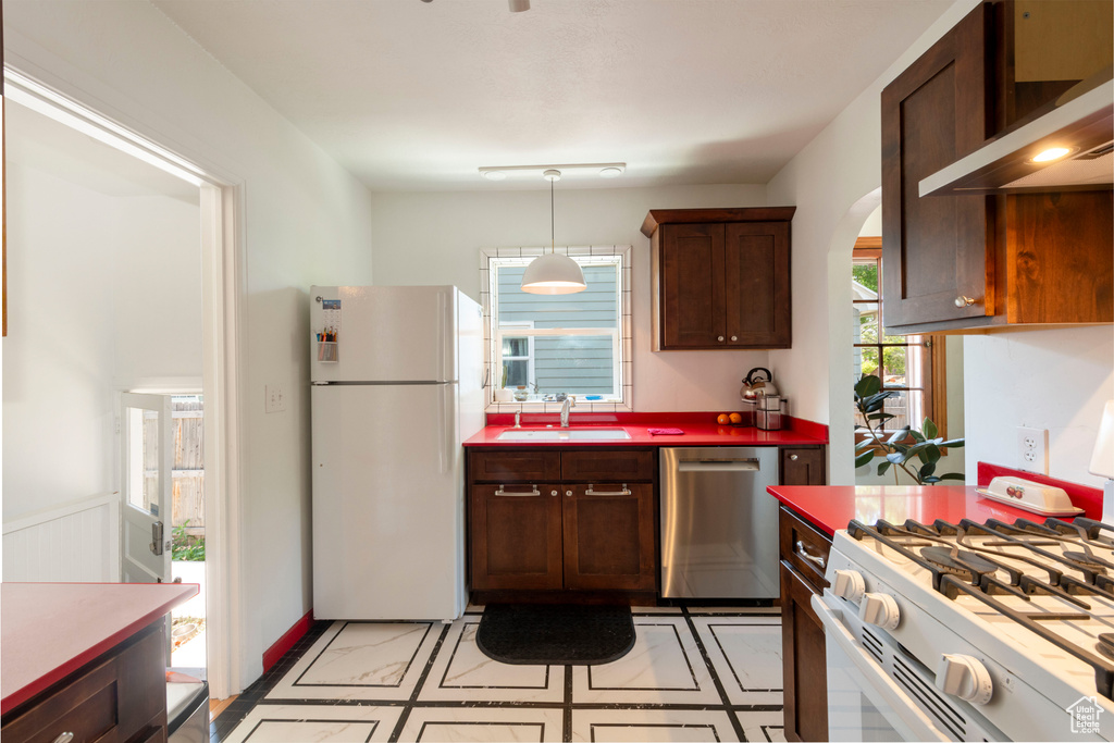 Kitchen featuring white appliances, wall chimney exhaust hood, pendant lighting, arched walkways, and dark brown cabinetry