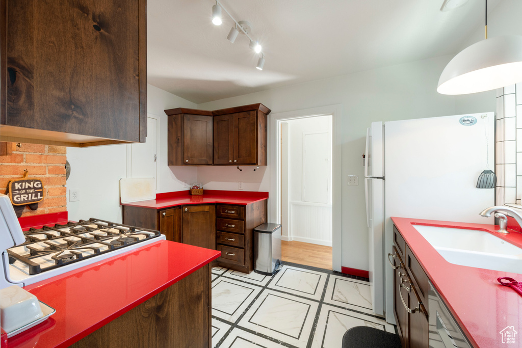 Kitchen with white gas stovetop, track lighting, light tile patterned floors, and dark brown cabinets