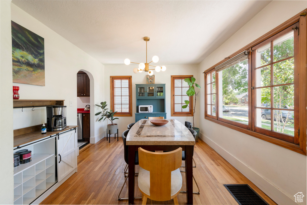 Dining area with a chandelier, light wood-type flooring, and arched walkways