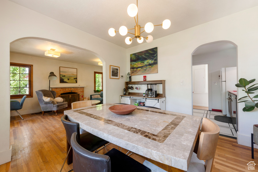 Dining space featuring arched walkways, light wood-type flooring, healthy amount of natural light, and a brick fireplace