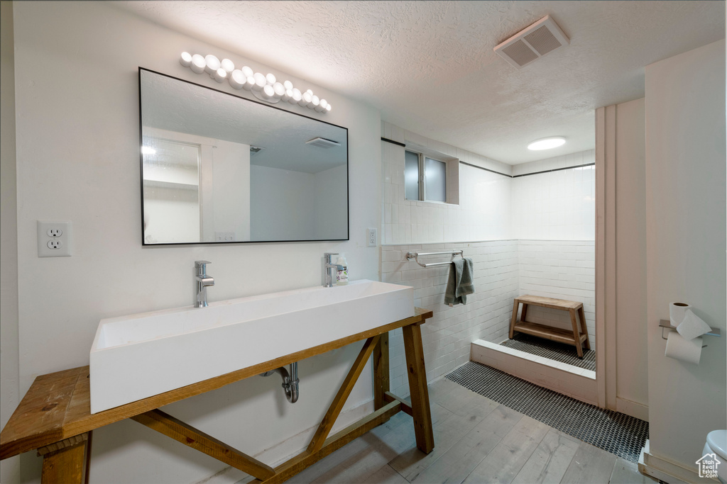 Bathroom with tile walls, wood finished floors, wainscoting, a textured ceiling, and a shower