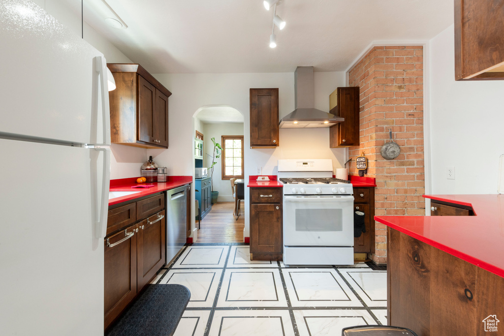 Kitchen featuring white appliances, wall chimney exhaust hood, and arched walkways