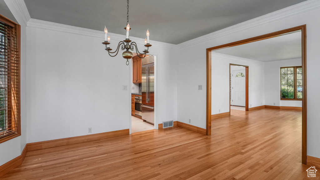 Empty room with light wood-type flooring, a chandelier, and ornamental molding