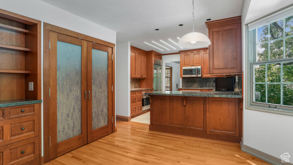 Kitchen with stainless steel microwave, brown cabinets, backsplash, light wood-style floors, and dark countertops