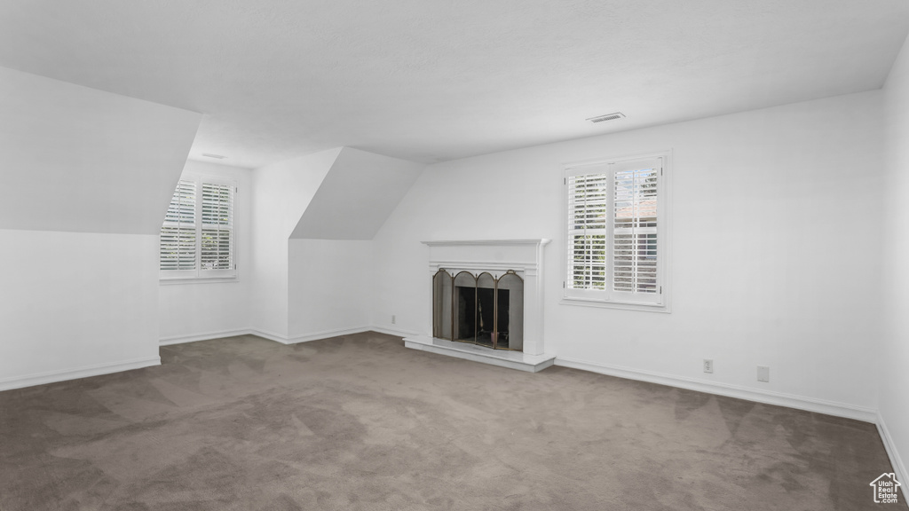 Unfurnished living room featuring carpet and a fireplace with raised hearth