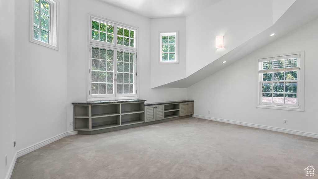 Unfurnished living room featuring light carpet, healthy amount of natural light, recessed lighting, and a towering ceiling