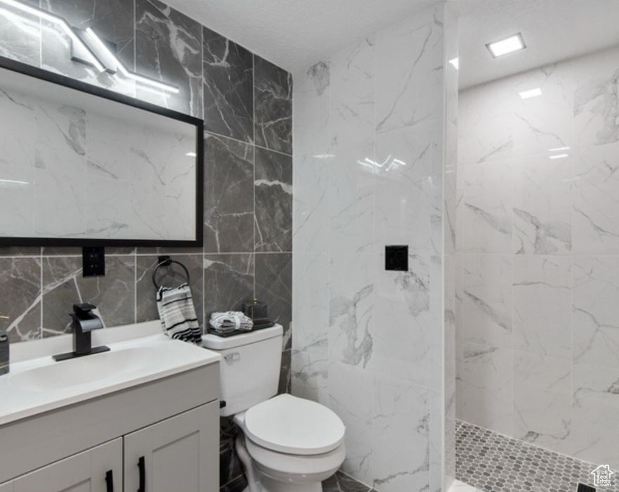 Bathroom featuring tile walls, vanity, a marble finish shower, toilet, and decorative backsplash