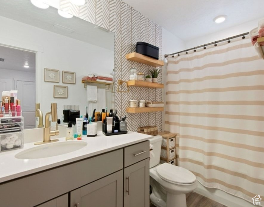 Bathroom with vanity, toilet, curtained shower, wood finished floors, and wallpapered walls