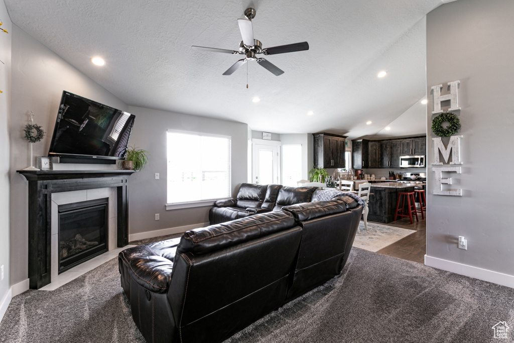 Living area featuring dark colored carpet, a ceiling fan, a fireplace with flush hearth, recessed lighting, and a textured ceiling
